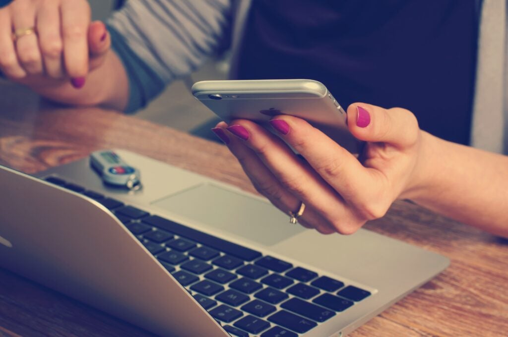 Image of person sitting at open laptop with mobile device in hand