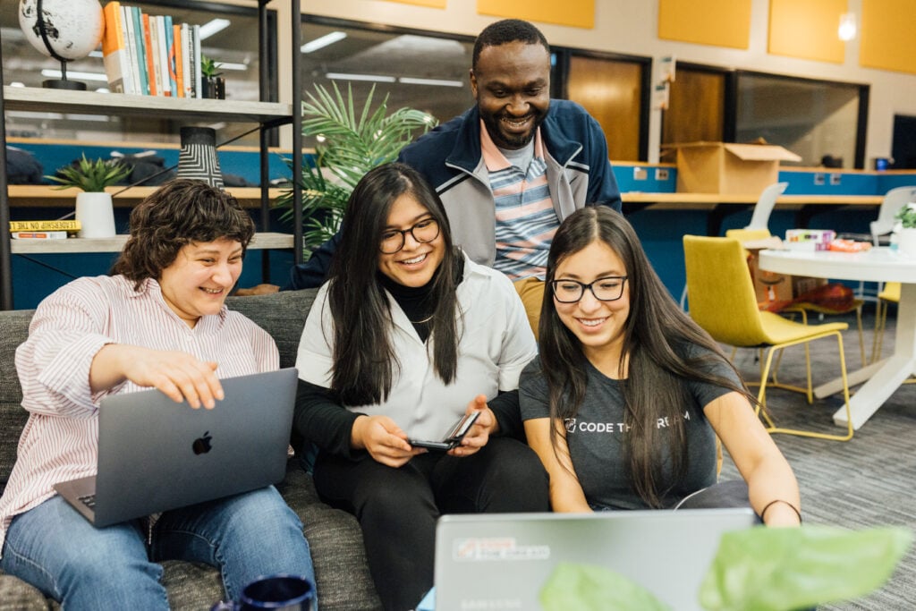 Four people looking at a computer and smiling