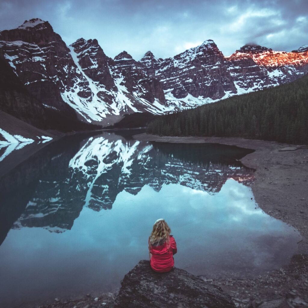 Woman looking at a lake with snow-covered mountains in the distance.